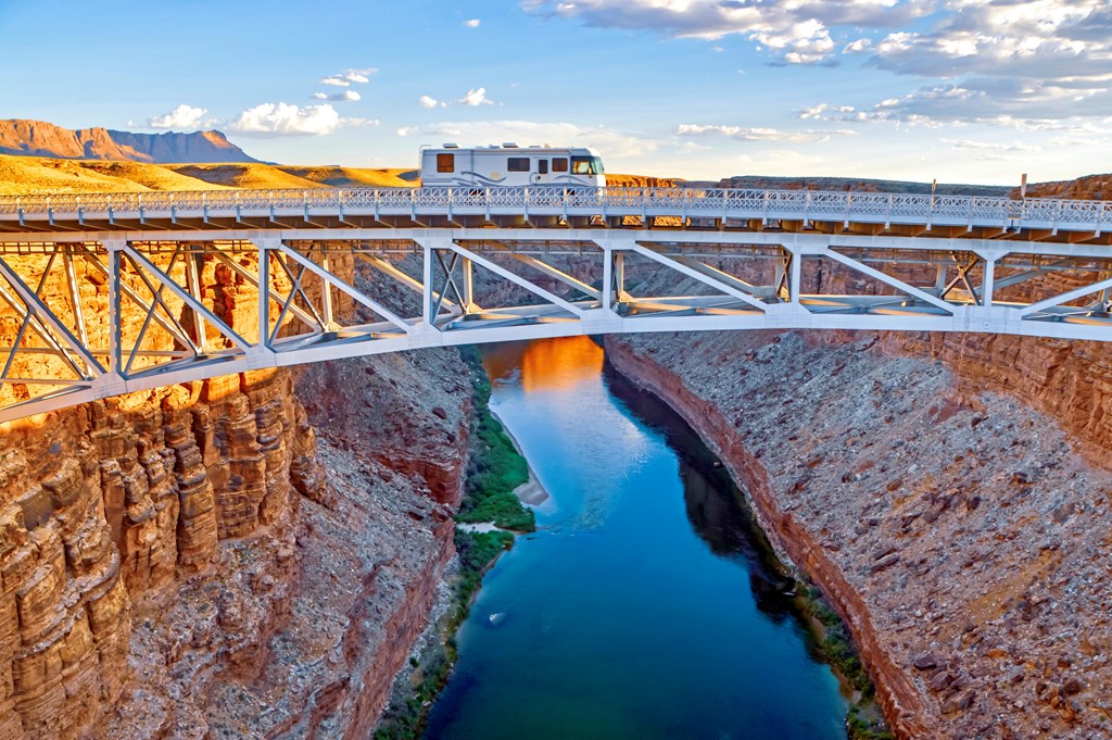 An RV crossing the colorado River on a high bridge over a red rock canyon.